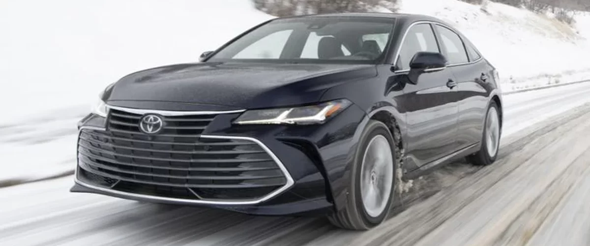 Toyota Avalon седан серебристого цвета на фоне городской застройки